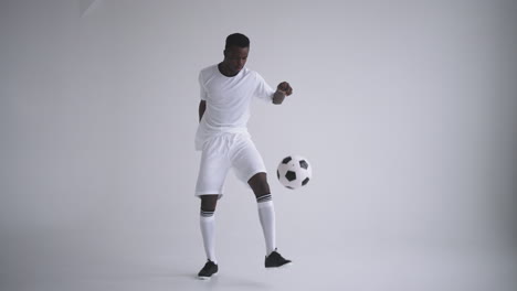 A-professional-black-football-player-in-a-white-uniform-on-a-white-background-juggles-a-ball-in-slow-motion.-African-American-ethnic-group-soccer-player-with-a-soccer-ball
